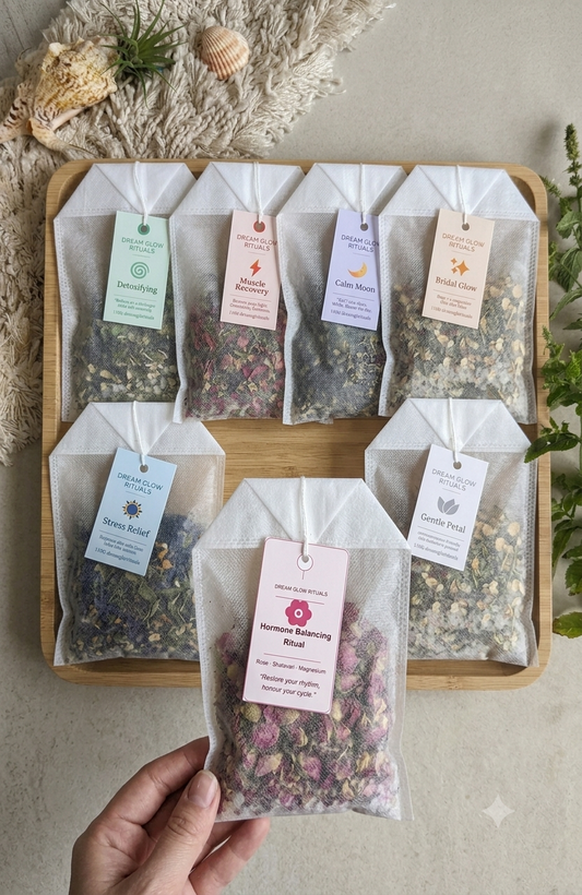 Herbal tea bags in clear packaging with tags on a wooden tray, held by a hand.