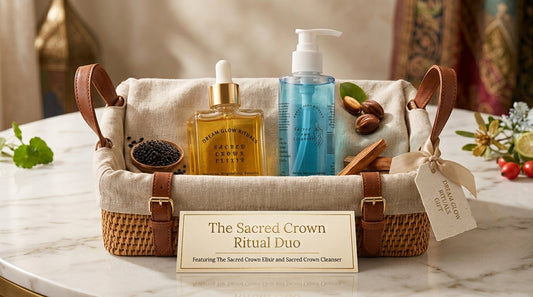 A gift basket set containing 'The Sacred Crown Ritual Duo' featuring a golden elixir bottle and a blue cleanser bottle, presented in a woven basket with leather handles on a marble table.