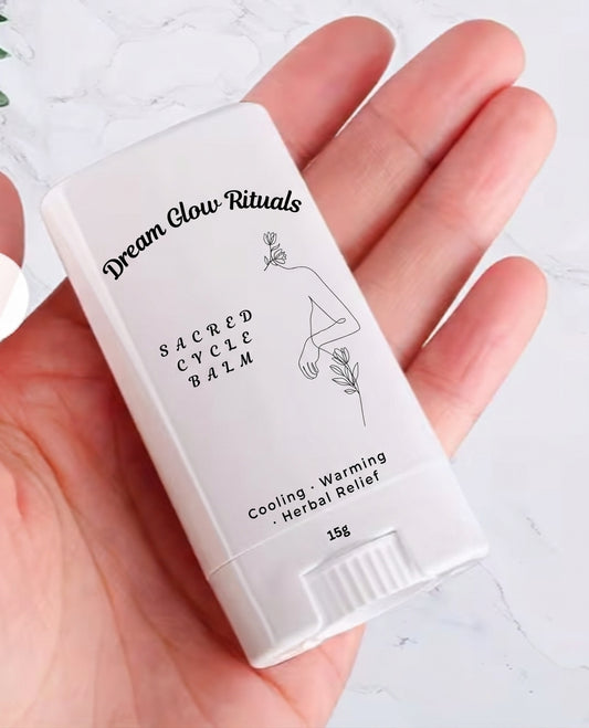 A hand holding a white stick container of Dream Glow Rituals Sacred Cycle Balm against a light marble background.