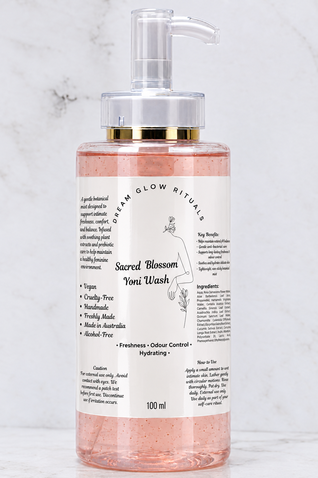 A 100ml bottle of Sacred Blossom Toni Wash by Dream Glow Rituals, featuring a clear pump dispenser with a gold collar and a white label, filled with pinkish-amber liquid, set against a light marble background.